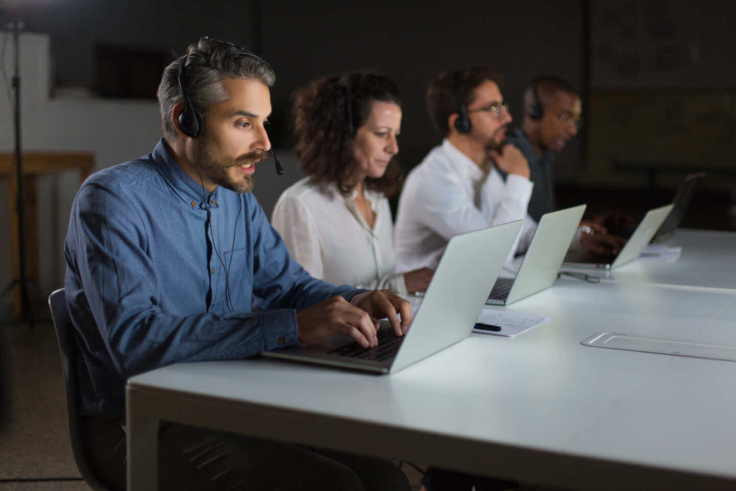 Team of call center agents working on laptops with headsets